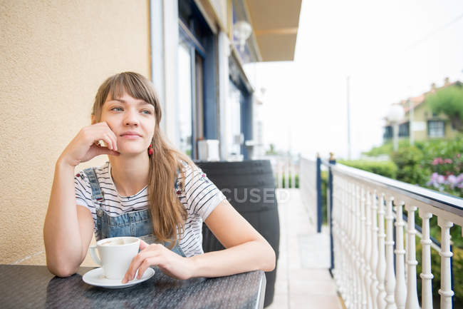 Thoughtful young woman sitting with coffee in outdoor cafe — Stock Photo