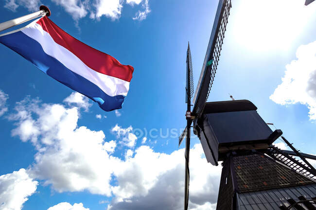 Von unten ein Foto der französischen Flagge, die in der Nähe der Mühle vor dem wolkenverhangenen Himmel weht. — Stockfoto