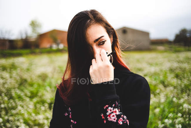Sensuale giovane donna in abito nero che tiene gli occhiali e in piedi in campo verde — Foto stock