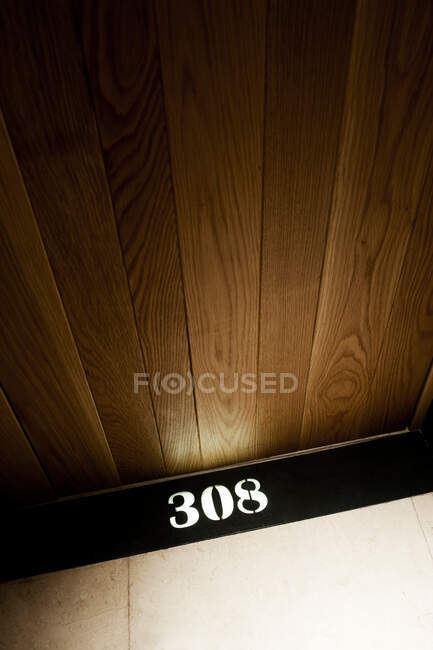Вид сверху на номер комнаты на черной доске, размещенной на паркете возле деревянной двери — стоковое фото