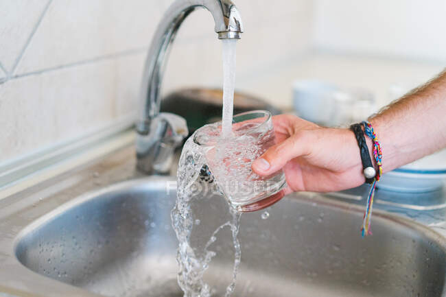 Crop main de personne méconnaissable laver le verre dans l'évier sur la cuisine. — Photo de stock
