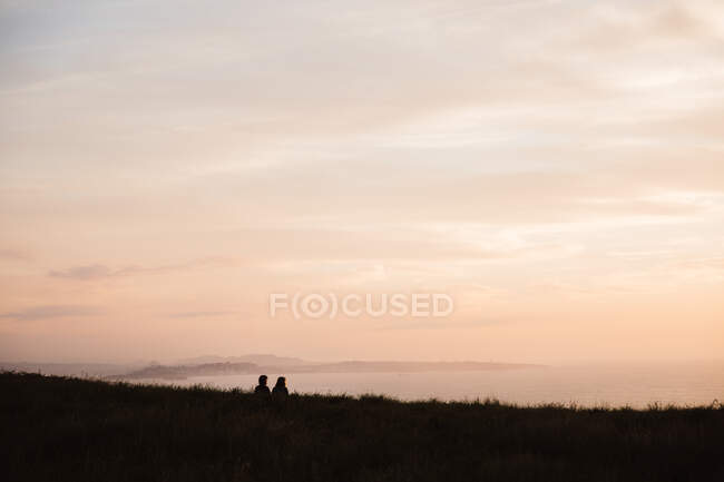 Back view of guys sitting on grass and looking picturesque sundown on sky background in Cantabria, Spain — Stock Photo