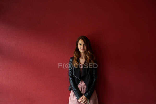 Jeune femme en veste debout près du mur rouge — Photo de stock