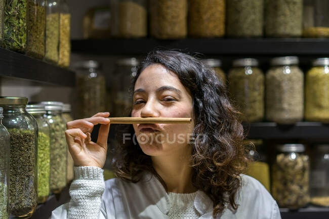 Pretty woman standing in spice shop and smelling cinnamon stick. — Foto stock