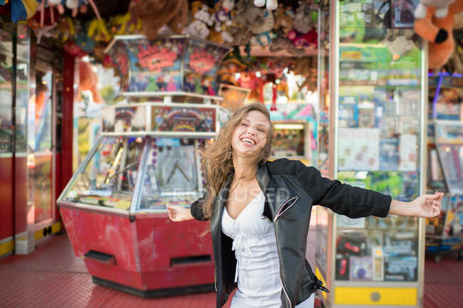 Jeune femme heureuse tournant autour dans la rue contre magasin de parc d'attractions — Photo de stock