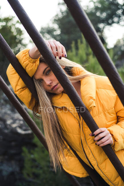 Молодая женщина с голубыми глазами и желтой курткой остается в природе положить голову на руку, глядя в камеру — стоковое фото