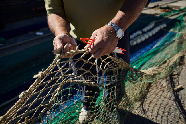 Ausschnitt von oben: Mann hält Fischernetz in den Händen und schneidet mit Messer — Stockfoto