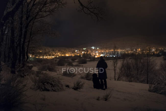 Чоловік і його домашня тварина ходять вночі в засніженому лісі в зимовий вечір — стокове фото