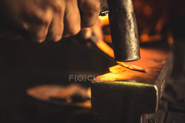 Anonymous man using hummer to forge blade from piece of metal in professional workshop — Stock Photo