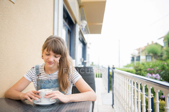 Усвідомлена молода жінка сидить з кавою у відкритому кафе — стокове фото
