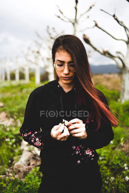 Young brunette woman in black outfit in glasses standing in field in overcast — Stock Photo