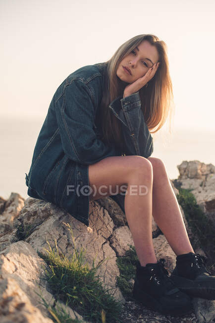 Mulher bonita relaxante em jeans jaqueta e tênis preto e segurando a cabeça no verão natureza — Fotografia de Stock