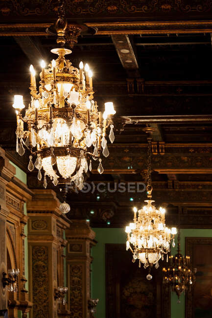 Burning ancient chandeliers hanging on ceiling of museum with patterned pillars and walls — Stock Photo