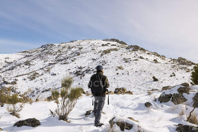 Jeune homme avec un sac à dos de randonnée profitant dans les montagnes enneigées par une journée ensoleillée d'hiver. — Photo de stock