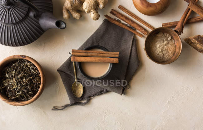 Чай с молоком, корицей, имбирем, белым перцем и кардамоном на бежевой поверхности — стоковое фото