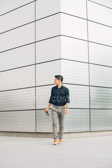 Hombre casual caminando frente a un edificio moderno y mirando hacia otro lado - foto de stock