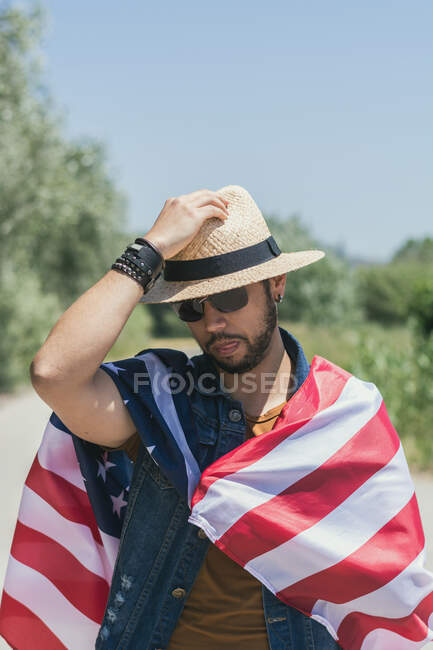 Человек счастлив и прыгает от радости с американским флагом на одинокой дороге — стоковое фото