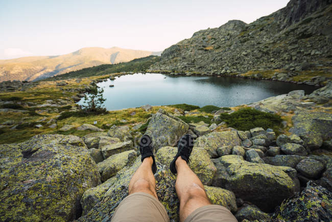 Cortado de pernas de homem sentado na margem do lago — Fotografia de Stock