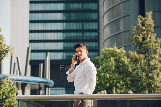 Young man talking on smartphone against modern skyscraper — Stock Photo