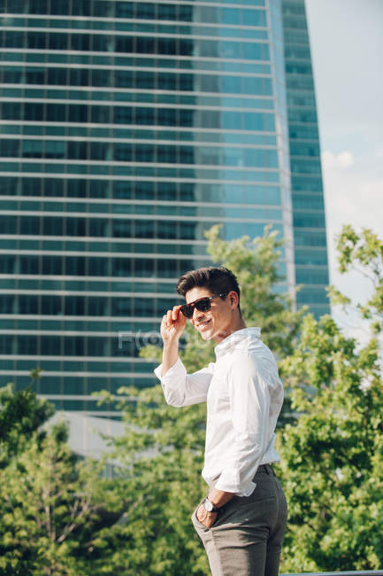 Un jeune homme d'affaires positif debout contre un gratte-ciel moderne — Photo de stock