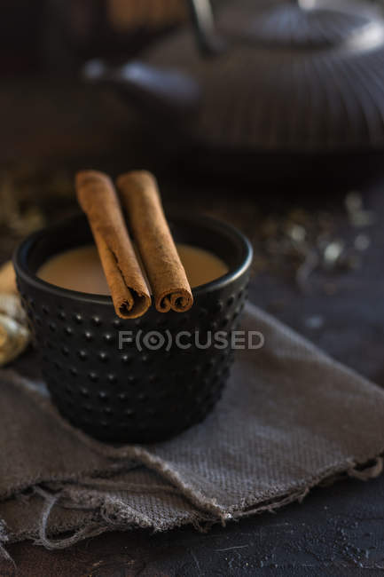 Tazza orientale di tè Chai con latte con cannella su stoffa grigia su sfondo scuro — Foto stock