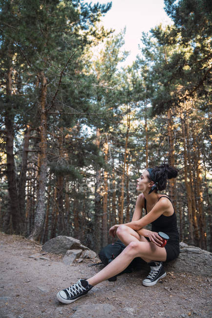 Очаровательная женщина с рюкзаком и чашкой в лесу — стоковое фото