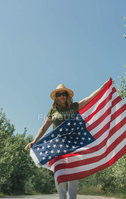Счастливая женщина, идущая с американским флагом и празднующая одинокую дорогу. Специальный день для празднования 4 июля — стоковое фото