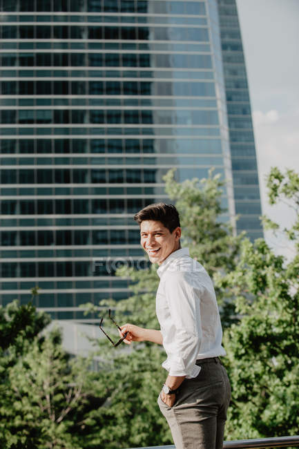 Rindo jovem empresário de pé contra edifício moderno e olhando sobre o ombro — Fotografia de Stock