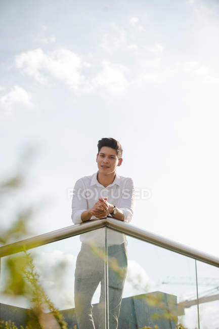 Young businessman leaning on railing outdoors and looking at camera — Stock Photo
