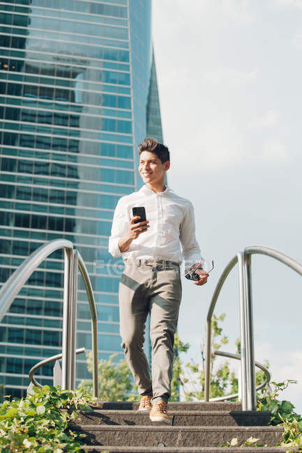 Cheerful man with smartphone walking down steps in modern city — Stock Photo
