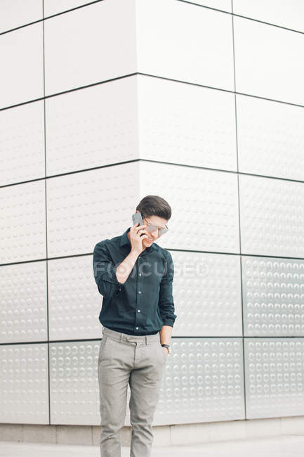 Joyeux jeune homme d'affaires parlant au téléphone contre le mur de construction — Photo de stock