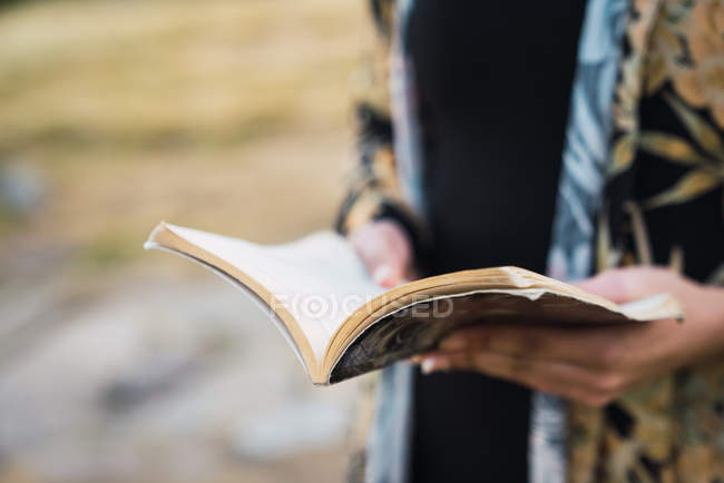 Primer plano de las manos de la mujer que sostiene el libro al aire libre - foto de stock