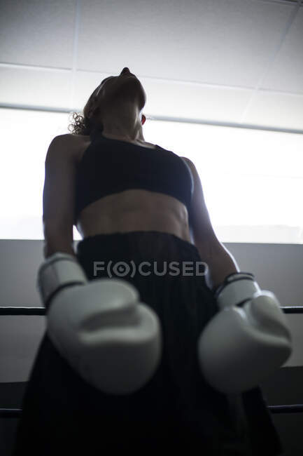 Lockige gesichtslose erwachsene Frau in schwarzer Sportkleidung, die in Schattierungen im Fitnessstudio nach oben schaut — Stockfoto