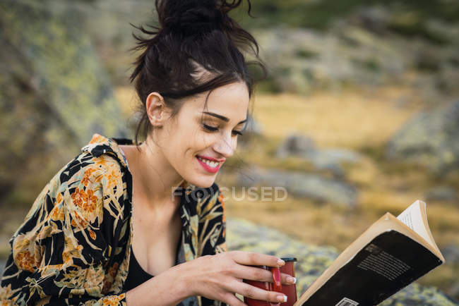 Jovem mulher muito sorridente ler livro sobre pedras enquanto viaja — Fotografia de Stock