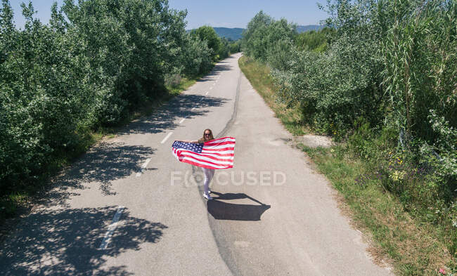 Eine Frau mit Hut geht mit der amerikanischen Flagge auf einer einsamen Straße. Besonderer Tag zur Feier des 4. Juli — Stockfoto