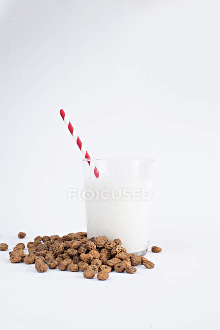 Haufen leckerer Rosinen und ein Glas frischer Milch mit gestreiftem Stroh auf weißem Hintergrund — Stockfoto