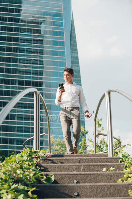 Elegant man with smartphone walking down steps in modern city — Stock Photo