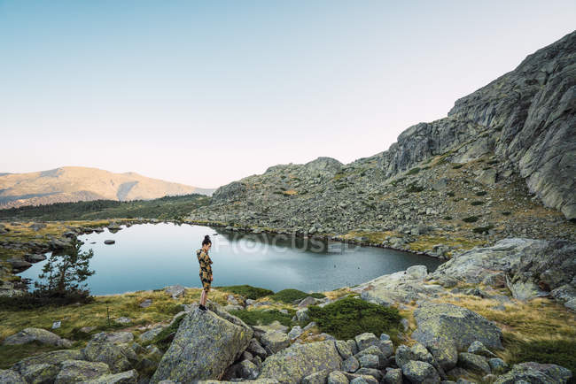 Donna che sta su rocce di piccolo lago in montagne — Foto stock