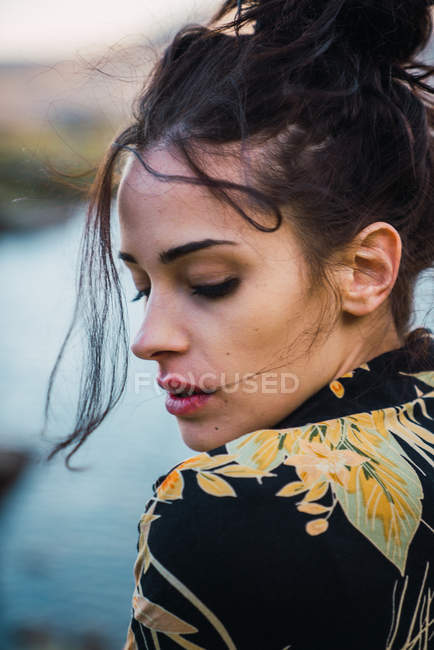 Young beautiful brunette in colorful shirt looking down with flying hair flocks in wind — Stock Photo