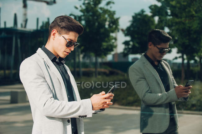 Young businessman using smartphone near glass wall — Stock Photo