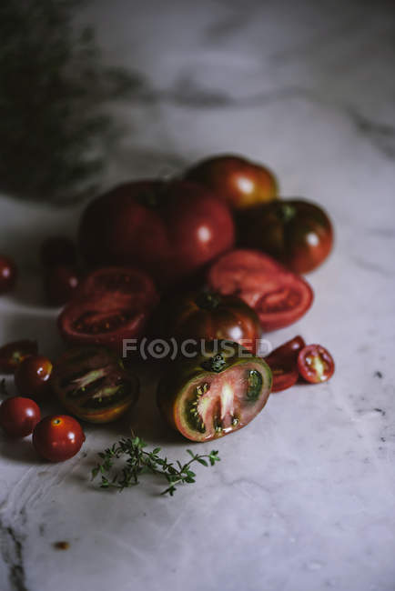 Fresh whole and halved tomatoes on white marble tabletop — Stock Photo