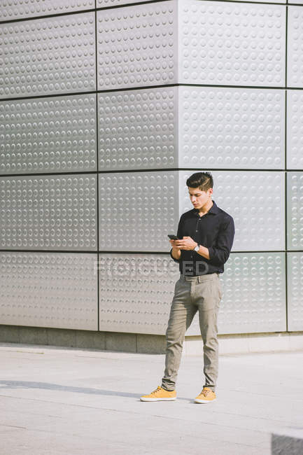 Eleganter Mann benutzt Handy, während er gegen Hauswand steht — Stockfoto