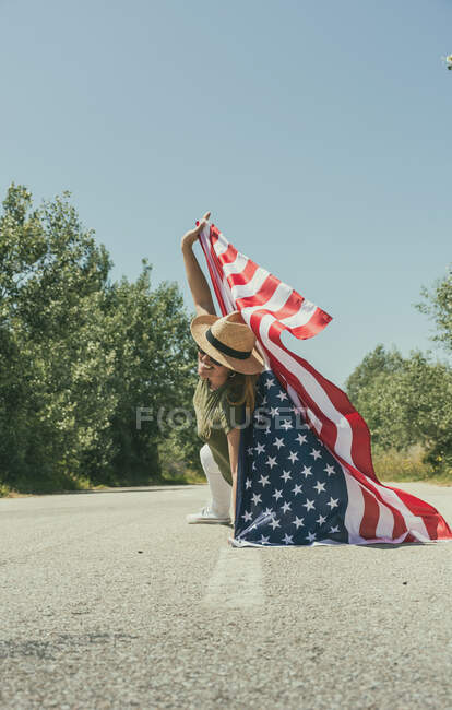 Happy woman walking with an american flag and celebrating on a lonely road. Special day to celebrate the 4th of July — Stock Photo