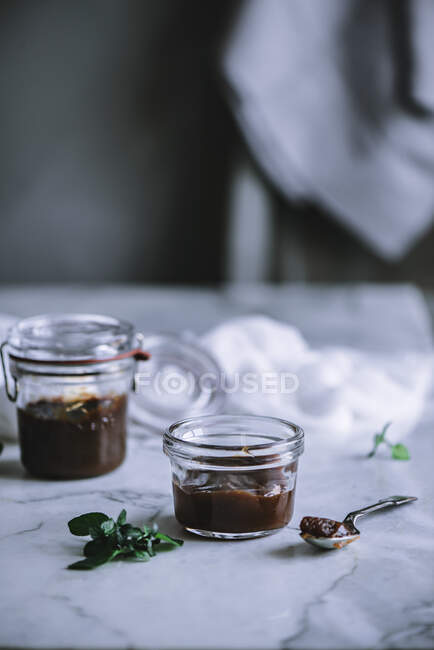 Löffel mit dicker Sauce auf Marmortischplatte in der Nähe von Glasgefäßen auf verschwommenem Hintergrund des stilvollen Zimmers liegend — Stockfoto