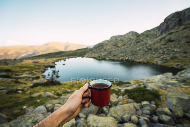 Cropped of hand of man with mug on shore of lake — Stock Photo