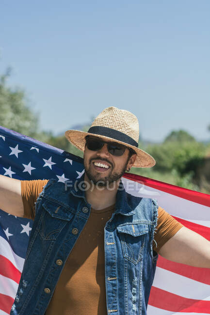 Homem feliz e pulando de alegria com uma bandeira americana em uma estrada solitária — Fotografia de Stock