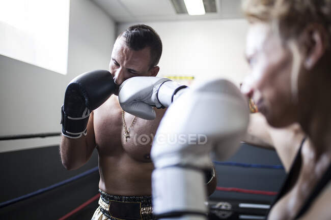 Man in sport shorts getting hit from woman in white gloves on ring in light athletic space — Stock Photo