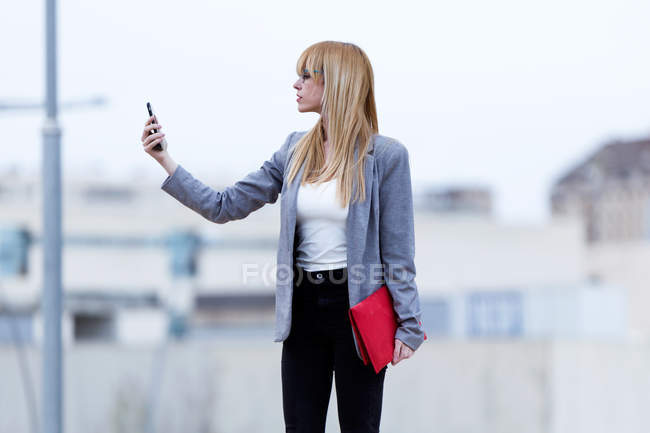 Young female blond taking selfie on street  blurred background — Stock Photo