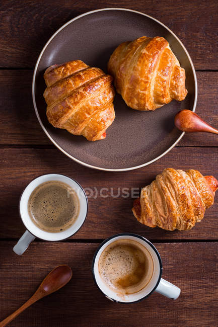 From above cups of coffee and croissants on plate on wooden table. — Stock Photo