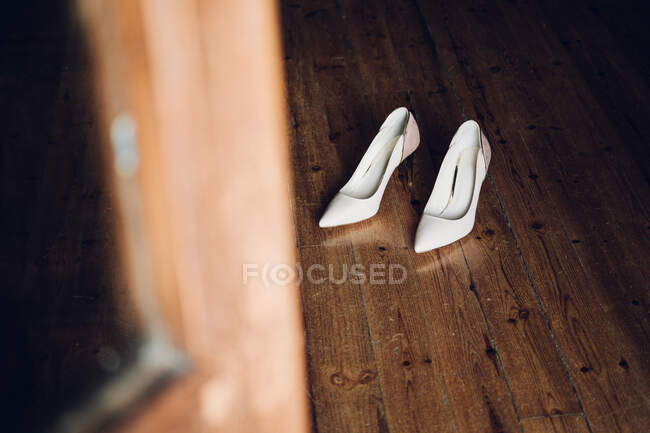 Desde arriba vista de los zapatos blancos nupciales poner en parquet marrón en la habitación - foto de stock